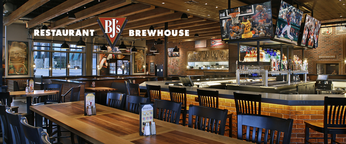 Inside of a BJs brewhouse and restaurant, with a large bar and sports displayed on the tv screens