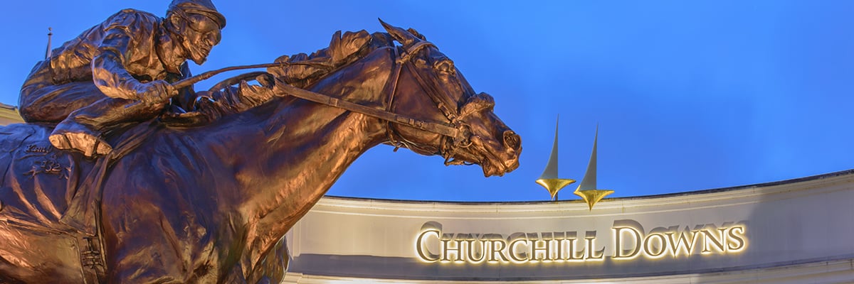 The Churchill Downs building sign with a bronze statue of a jockey on a horse in the foreground