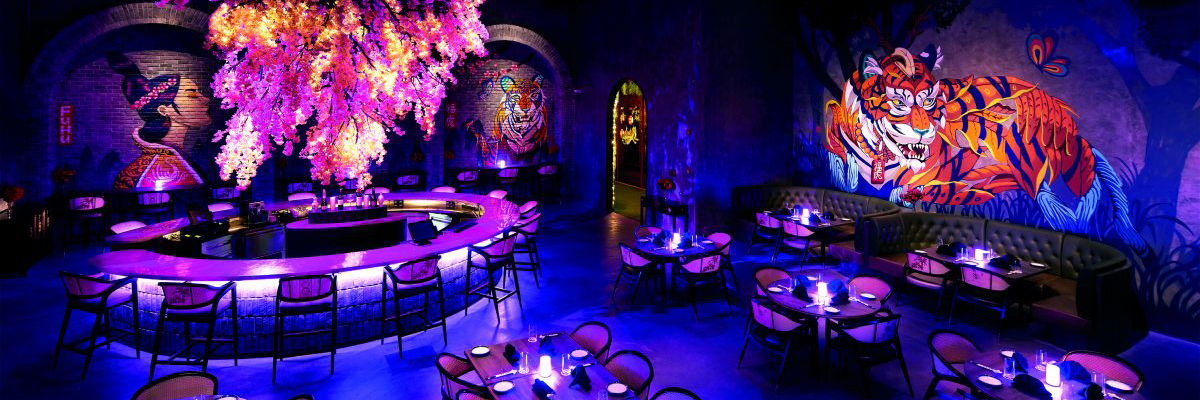 Image of a nightlife building with dining tables illuminated by a purple aura