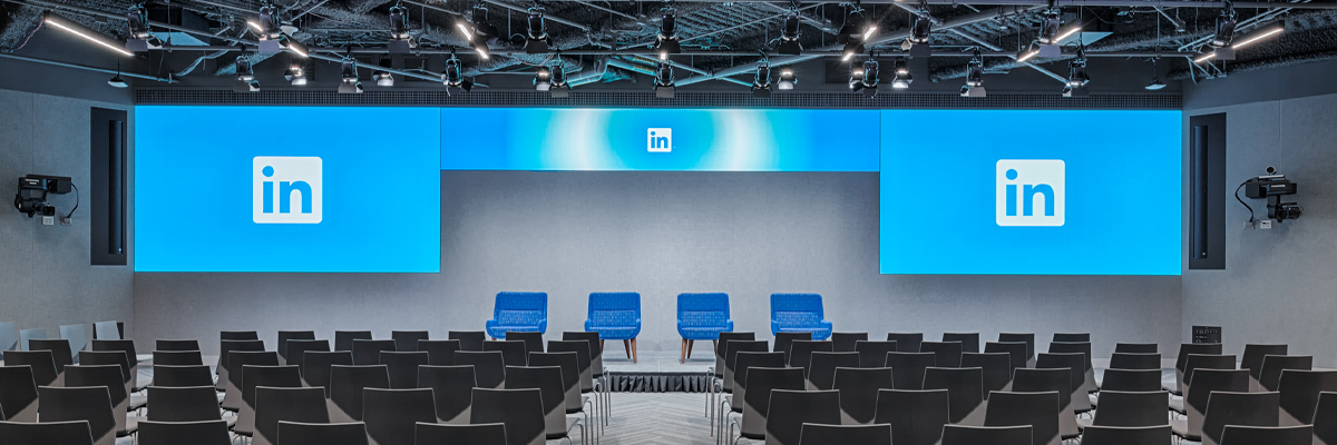 One of LinkedIns large meeting rooms in on of their corperage campuss, with rows of chars and large screens displaying their logo